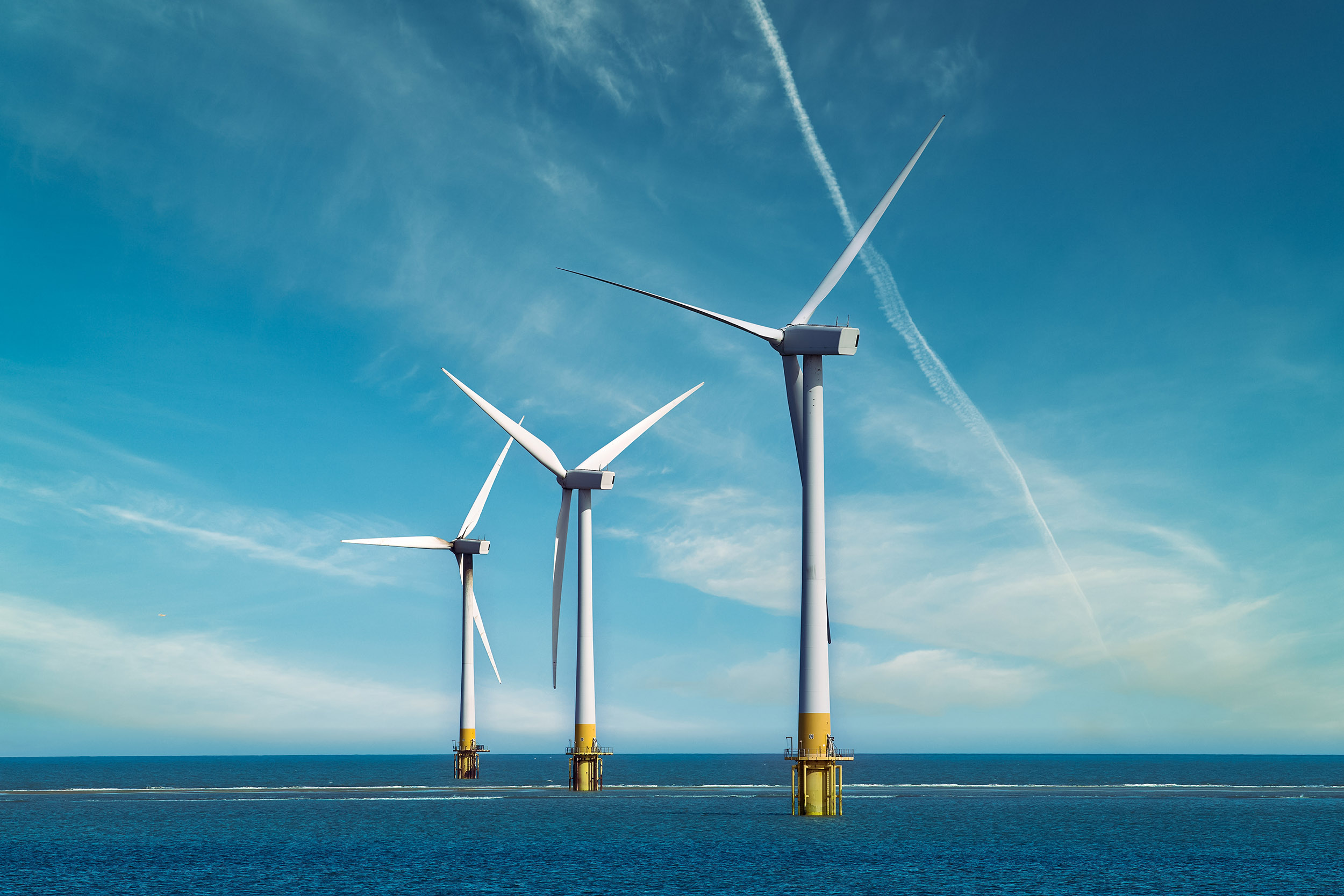 Three Offshore Wind Turbines Standing In The Sea, With Clear Blue Sky. Wind Turbines At Sea.